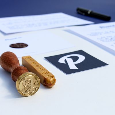 A custom gold wax seal made from the Penned logo, shown with its laser-engraved die